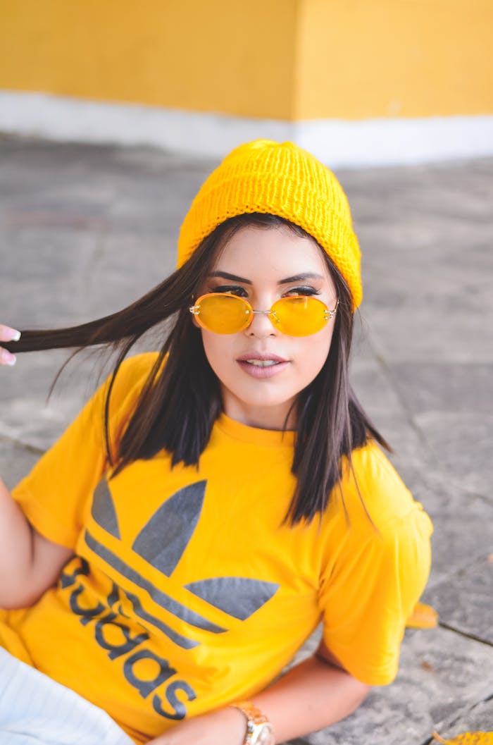 Trendy woman sports yellow streetwear with sunglasses and beanie for a vibrant, stylish look.